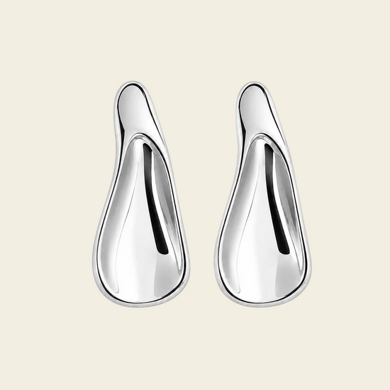 A pair of polished silver teardrop-shaped earrings with a smooth, reflective finish, displayed on a light beige background.