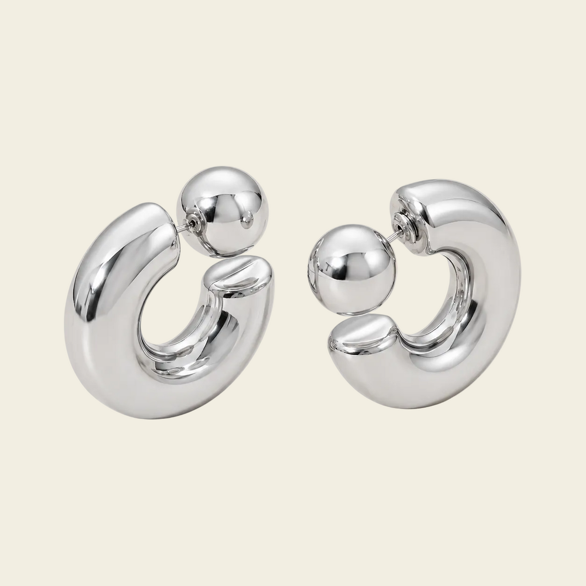 A pair of polished silver-toned hoop earrings with a small spherical bead detail at the top, displayed on a solid light beige background.