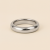 A polished silver band ring with a smooth, rounded profile, photographed on a clean, solid, warm beige background.