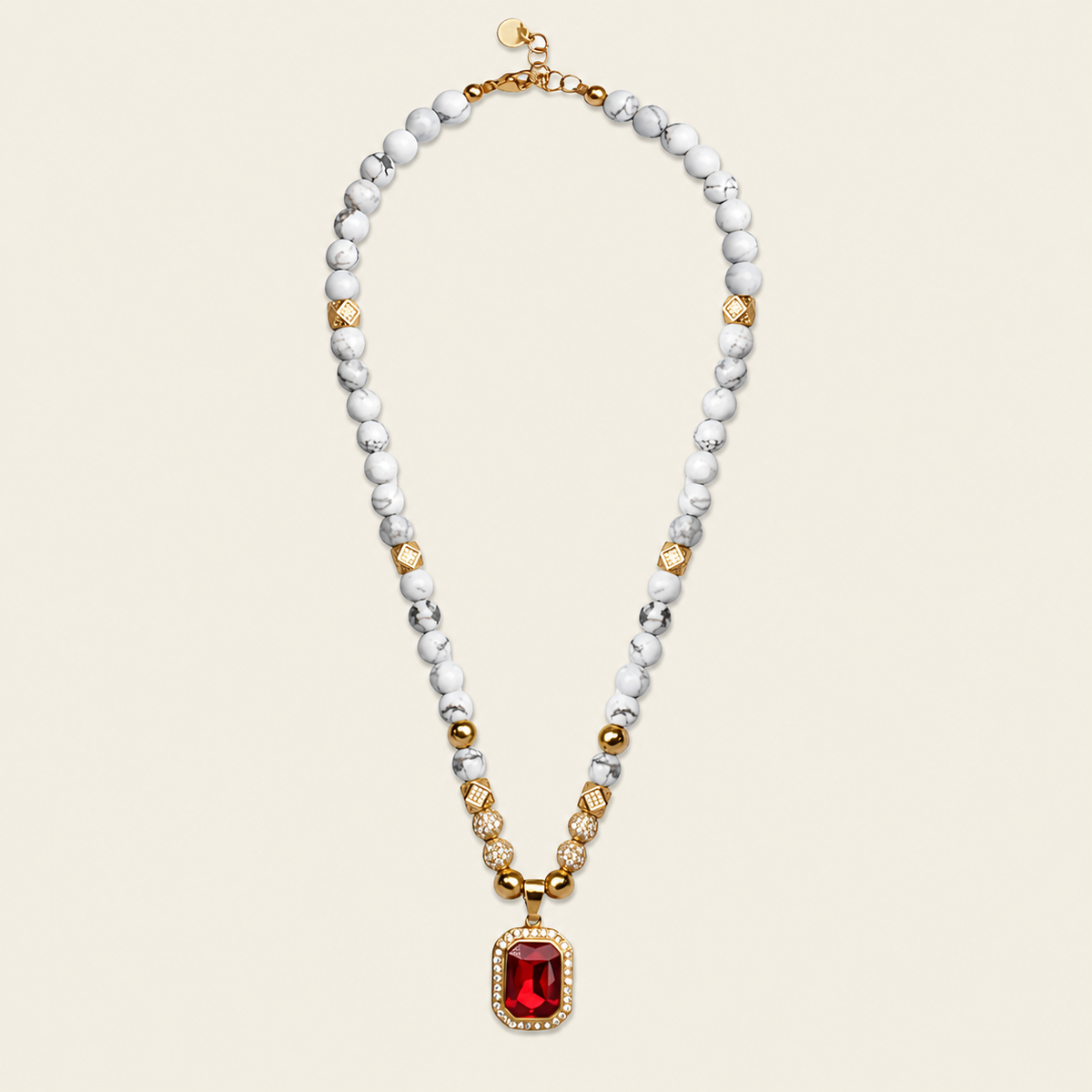 A beaded necklace featuring white and gray marbled beads, accented with gold spacer beads and a central rectangular red gemstone pendant with a gold border, set against a solid light beige background.