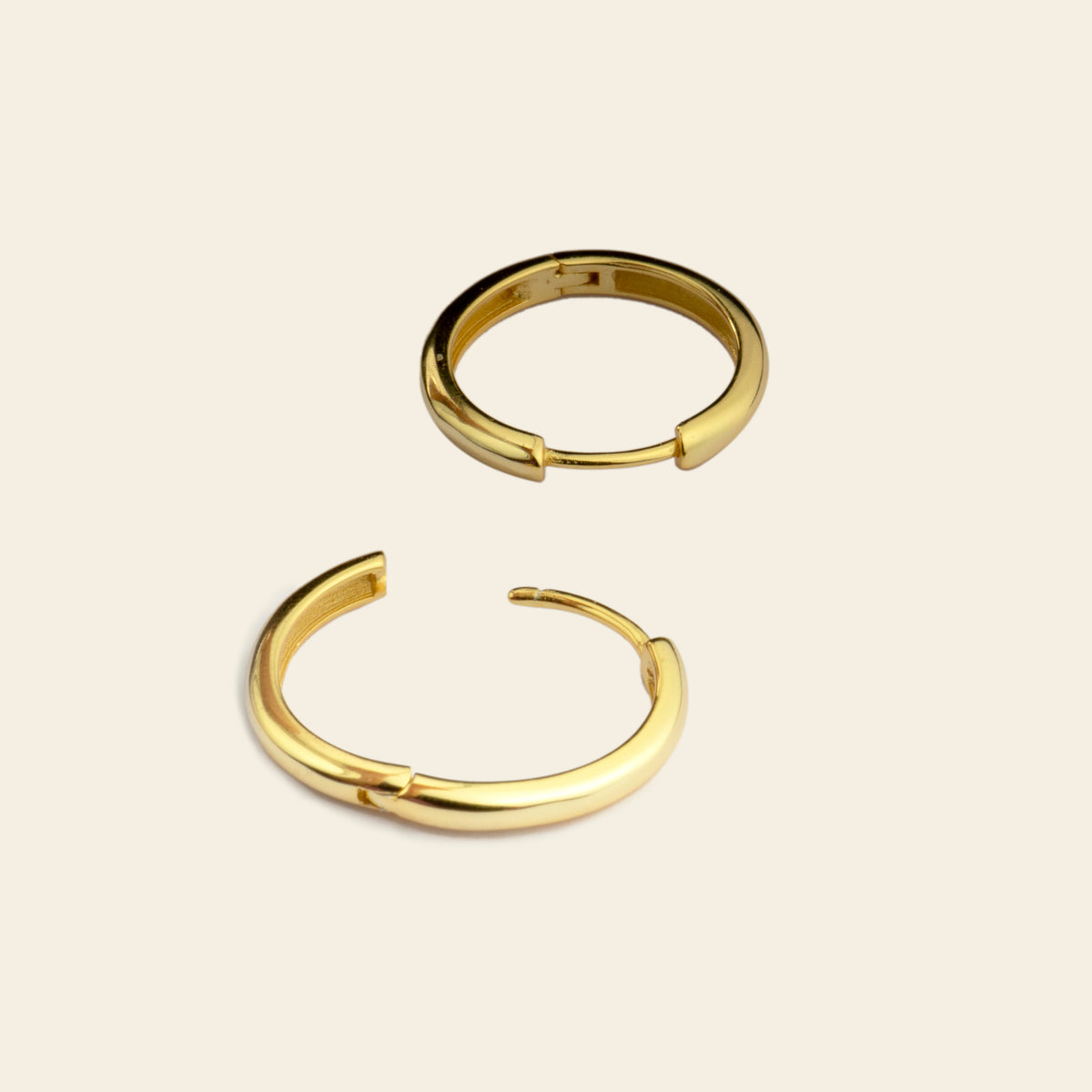Two gold hoop earrings on a beige background