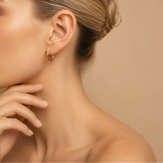 Close-up of a person wearing gold hoop earrings with a neutral background