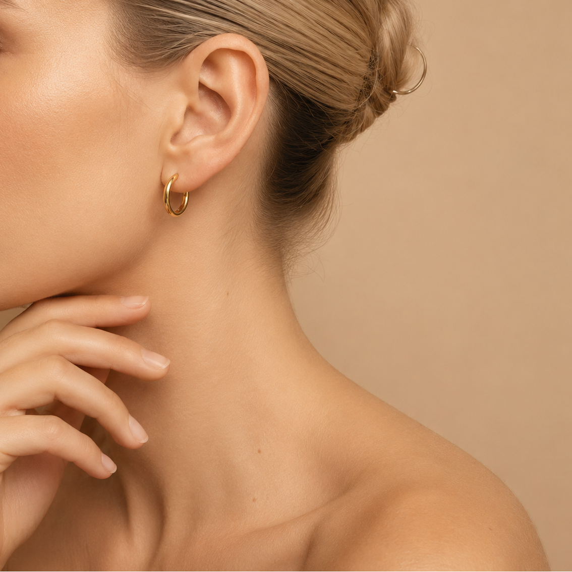 Close-up of a person wearing gold hoop earrings with a neutral background