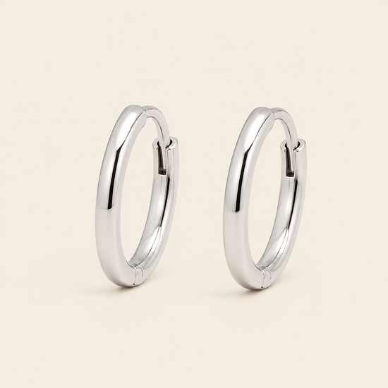A pair of polished silver hoop earrings shown on a clean, solid, light beige background.