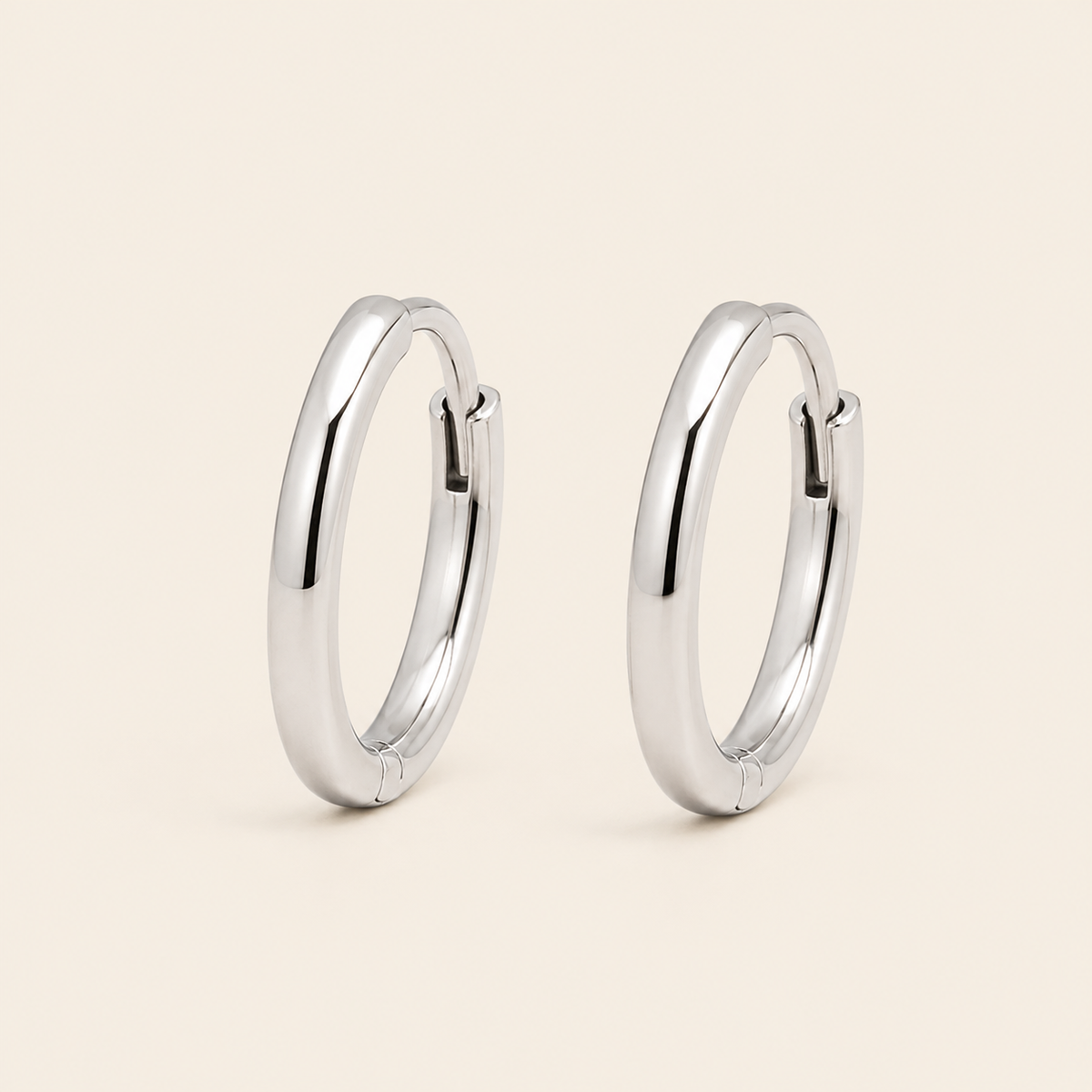 A pair of polished silver hoop earrings shown on a clean, solid, light beige background.