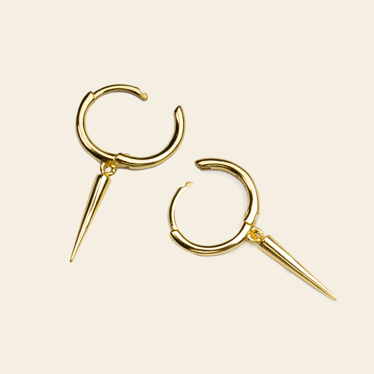Gold hoop earrings with spike details on a beige background
