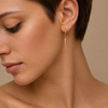 Close-up of a woman wearing a gold earring against a neutral background