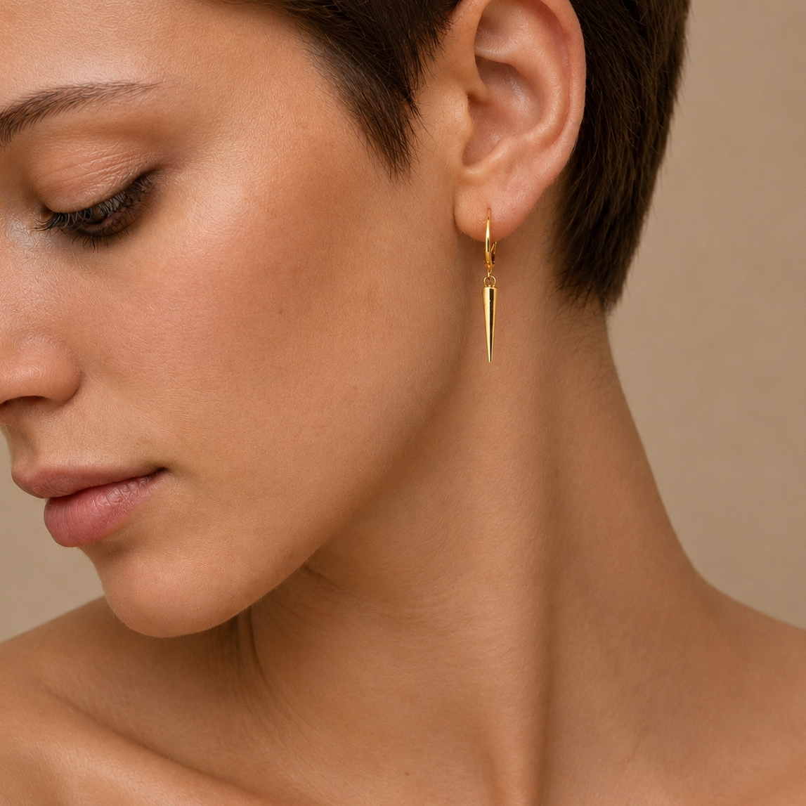 Close-up of a woman wearing a gold earring against a neutral background