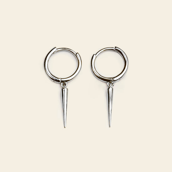 Pair of silver hoop earrings with spike extensions on a beige background