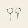 Pair of silver hoop earrings with spike extensions on a beige background