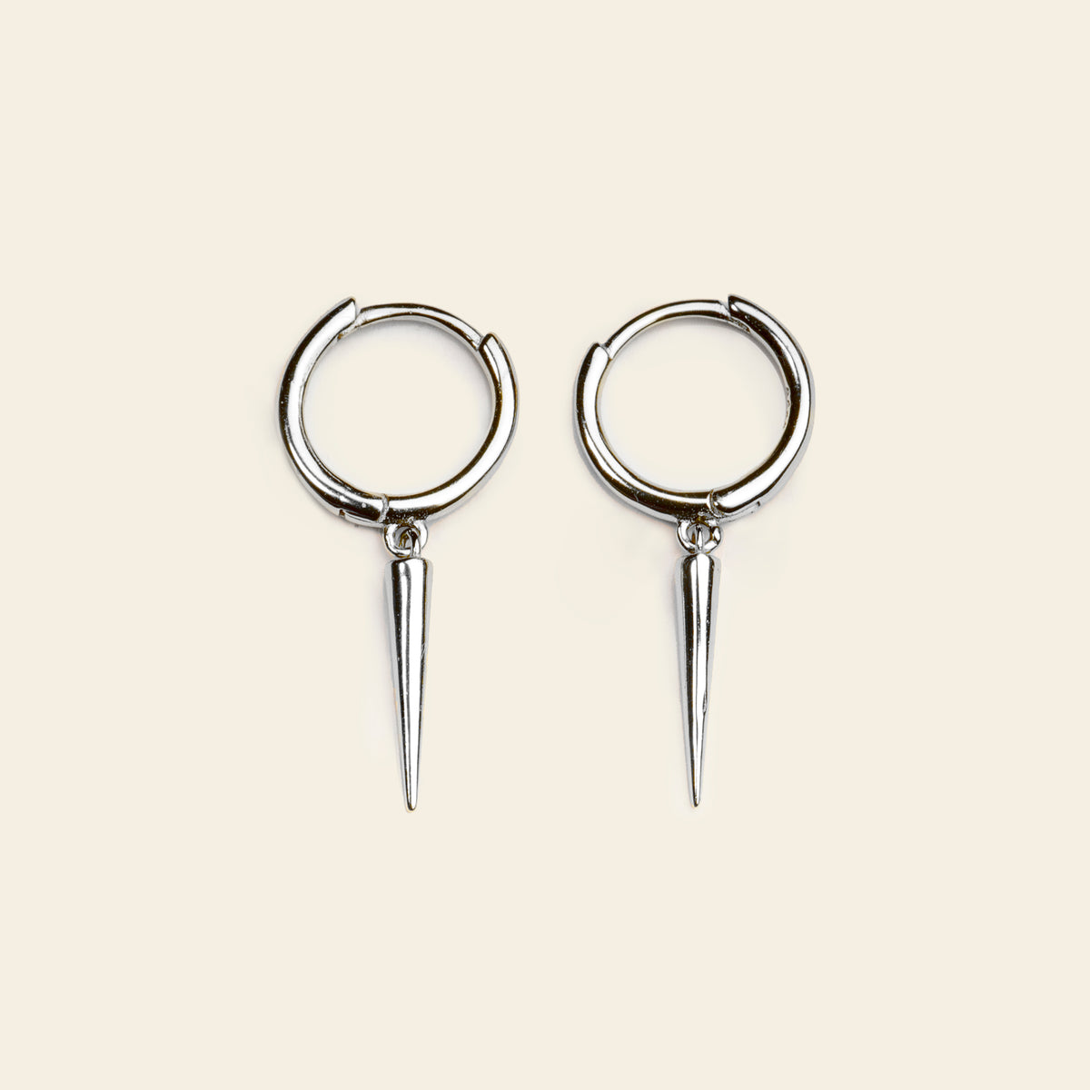 Pair of silver hoop earrings with spike extensions on a beige background