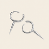 A pair of silver-toned hoop earrings with sharp spike charms, displayed on a solid light beige background.