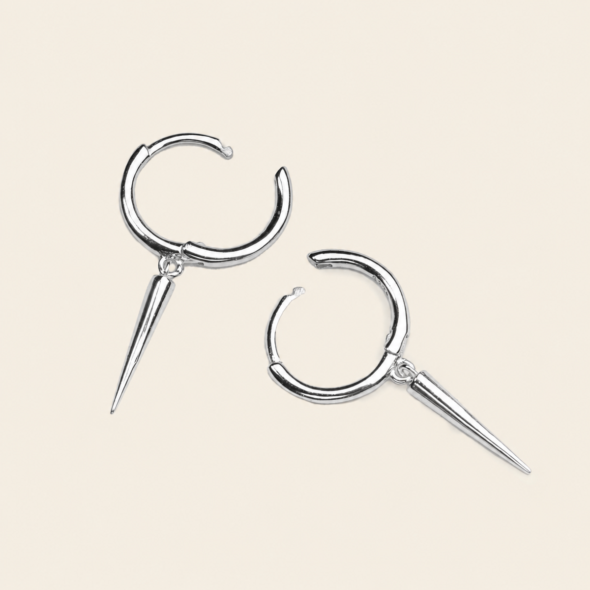 A pair of silver-toned hoop earrings with sharp spike charms, displayed on a solid light beige background.