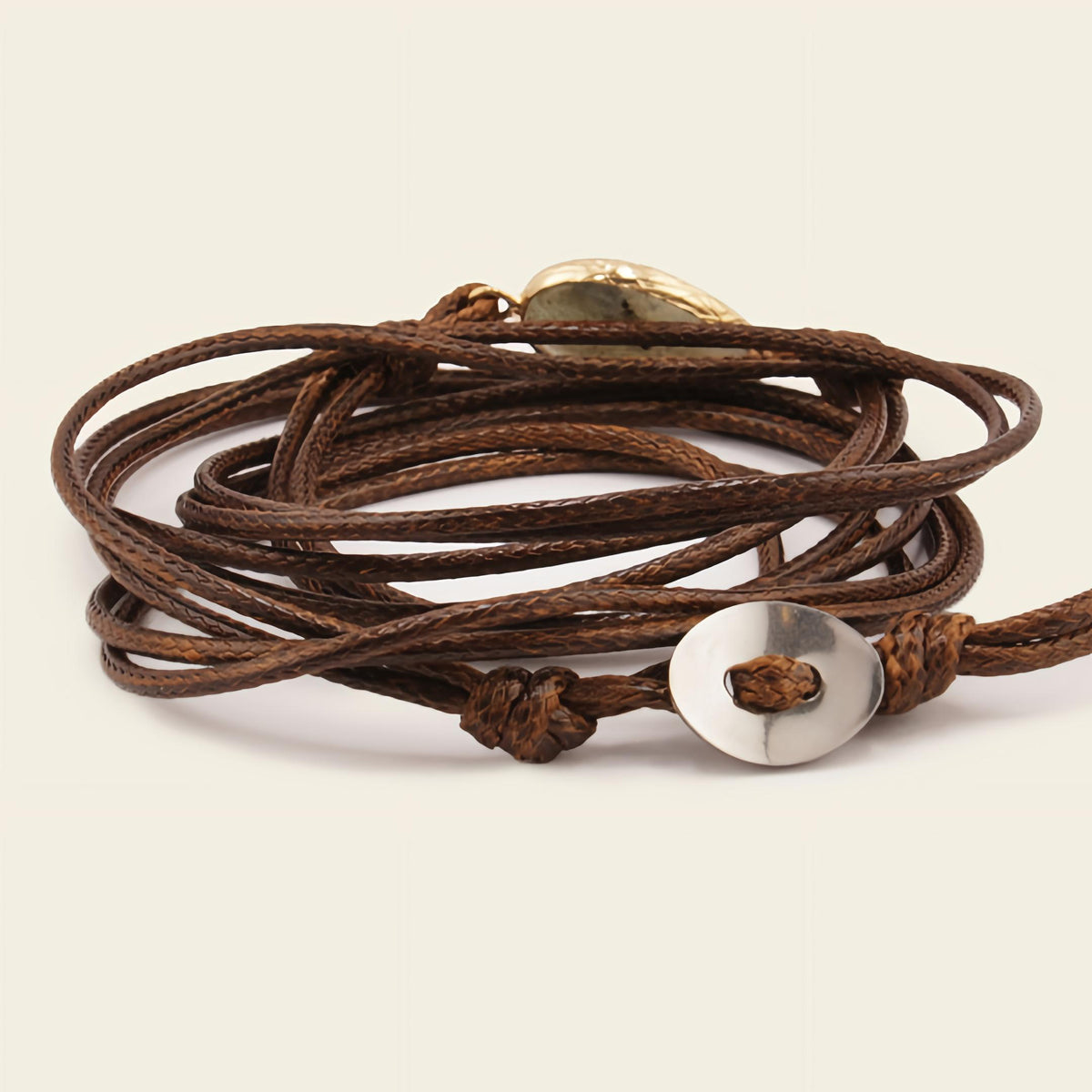 Brown leather wrap bracelet with a silver button clasp on a beige background