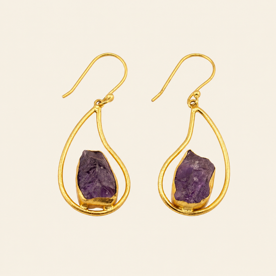 Gold earrings with purple gemstones on a beige background