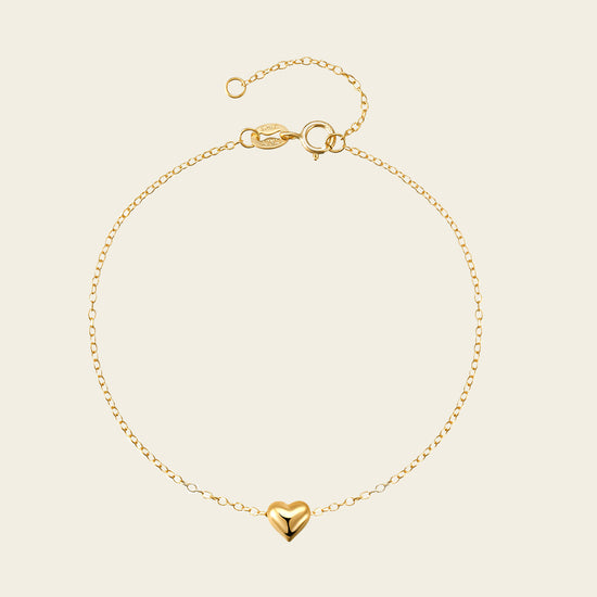 Gold bracelet with a heart charm on a beige background