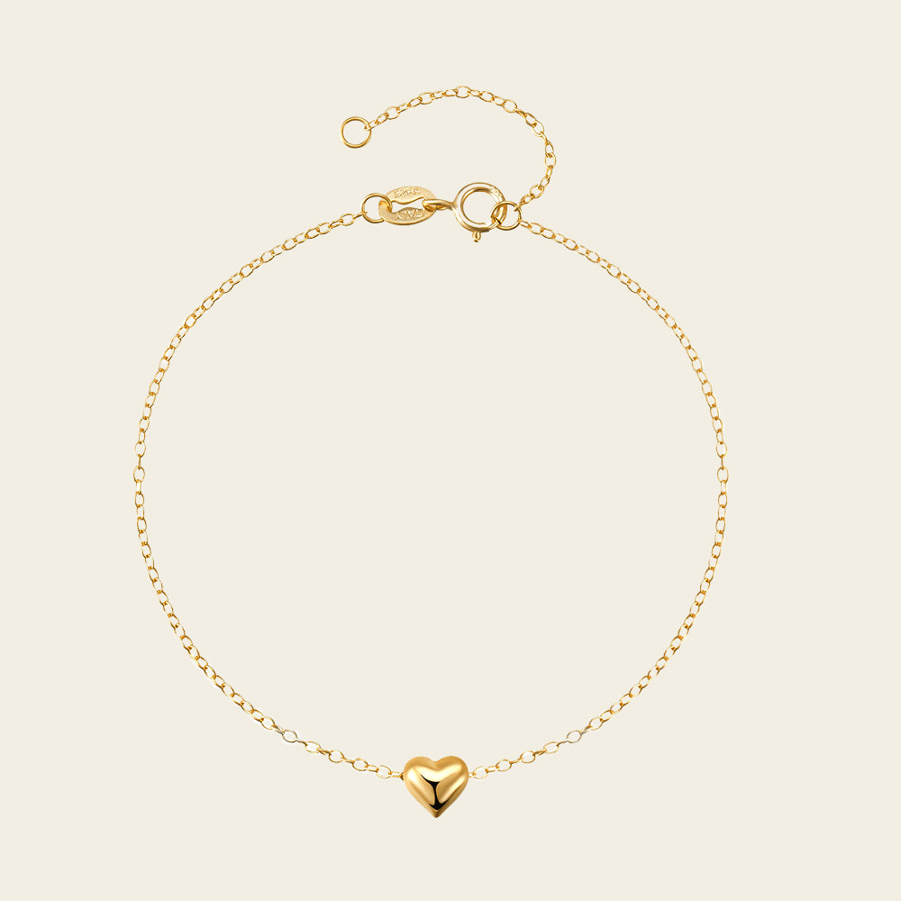 Gold bracelet with a heart charm on a beige background