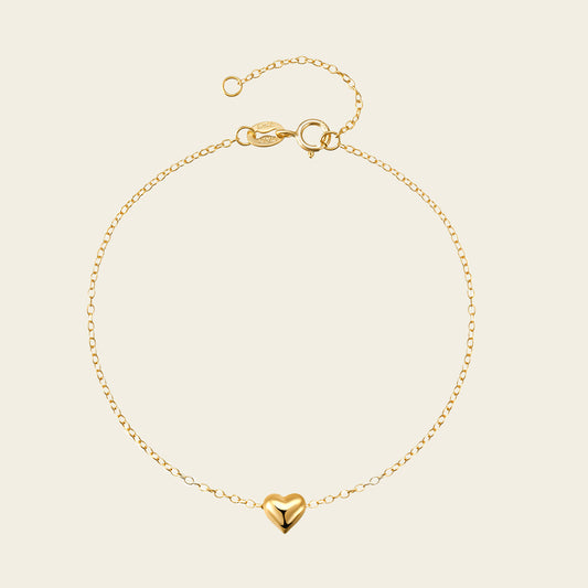 Gold bracelet with a heart charm on a beige background