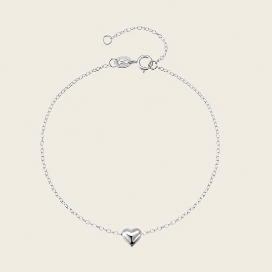 Silver bracelet with a heart-shaped charm on a beige background