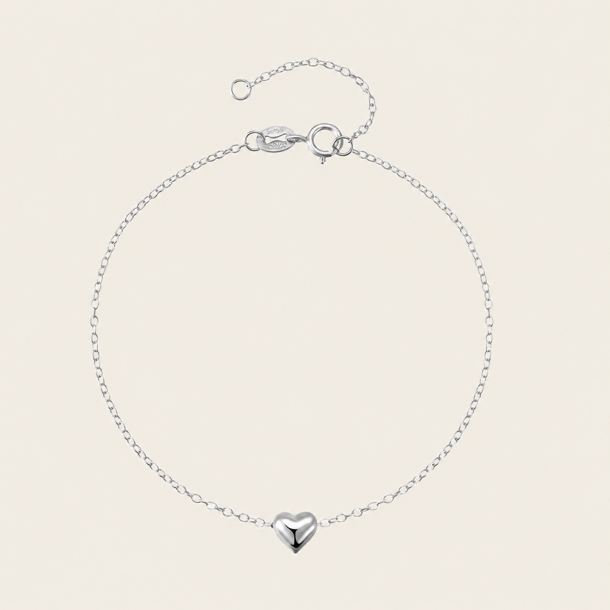 Silver bracelet with a heart-shaped charm on a beige background