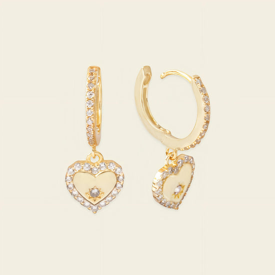 Gold hoop earrings with heart-shaped charms on a beige background