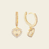 Gold hoop earrings with heart-shaped charms on a beige background