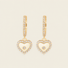 Gold heart-shaped earrings with diamond accents on a beige background