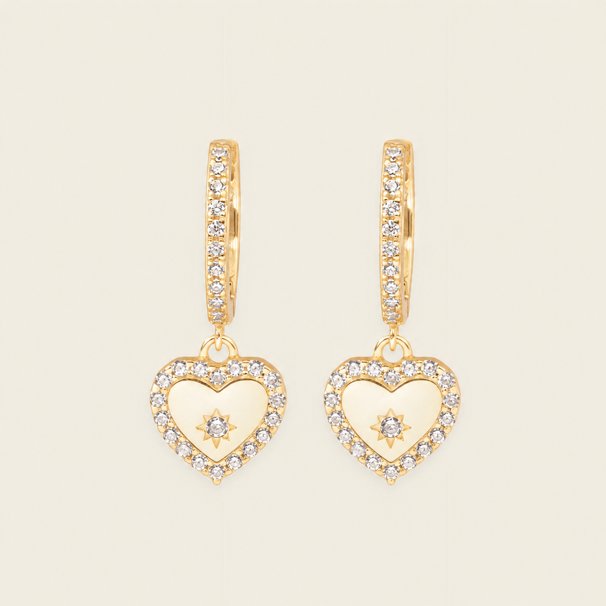 Gold heart-shaped earrings with diamond accents on a beige background