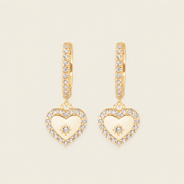 Gold heart-shaped earrings with diamond accents on a beige background