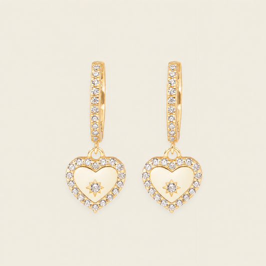 Gold heart-shaped earrings with diamond accents on a beige background