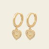 Gold hoop earrings with heart-shaped charms on a beige background