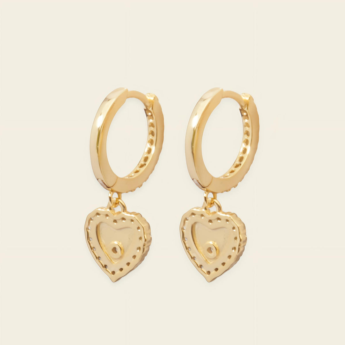 Gold hoop earrings with heart-shaped charms on a beige background