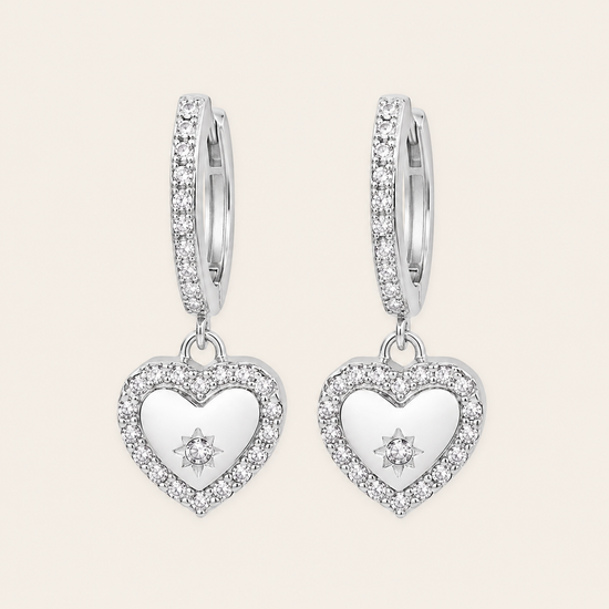 Heart-shaped silver earrings with clear stones on a light gray background