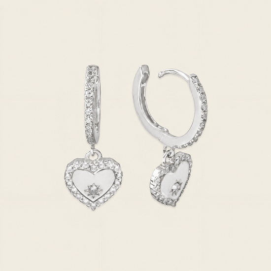Silver heart-shaped earrings with clear stones on a beige background