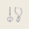 Silver heart-shaped earrings with clear stones on a beige background