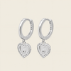 Silver hoop earrings with heart-shaped charms on a light beige background