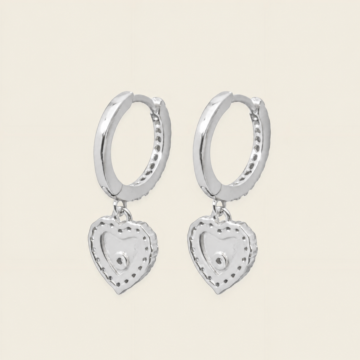 Silver hoop earrings with heart-shaped charms on a light beige background