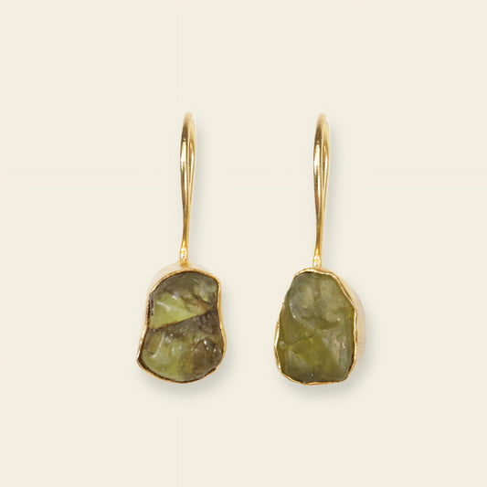 Pair of gold earrings with green stone drops on a beige background