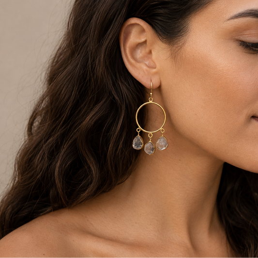 Close-up of a woman wearing gold hoop earrings with dangling stones.