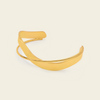 A polished gold-toned metal cuff bracelet with a smooth, curved open design, displayed on a solid light beige background.