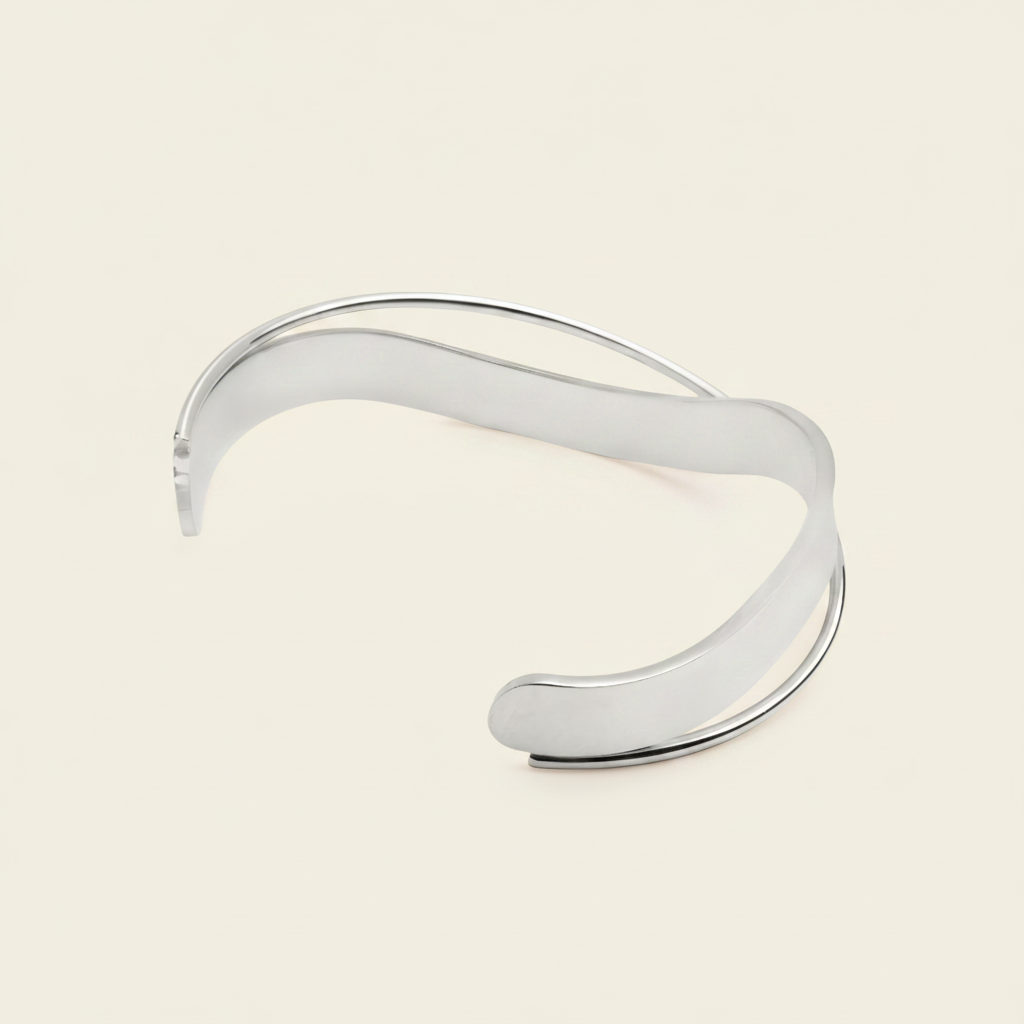A polished silver-tone open cuff bracelet with a smooth, flowing wavy design, displayed on a light cream background.