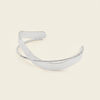 A polished silver-toned metal cuff bracelet with a smooth, curved open design, displayed on a solid light beige background.