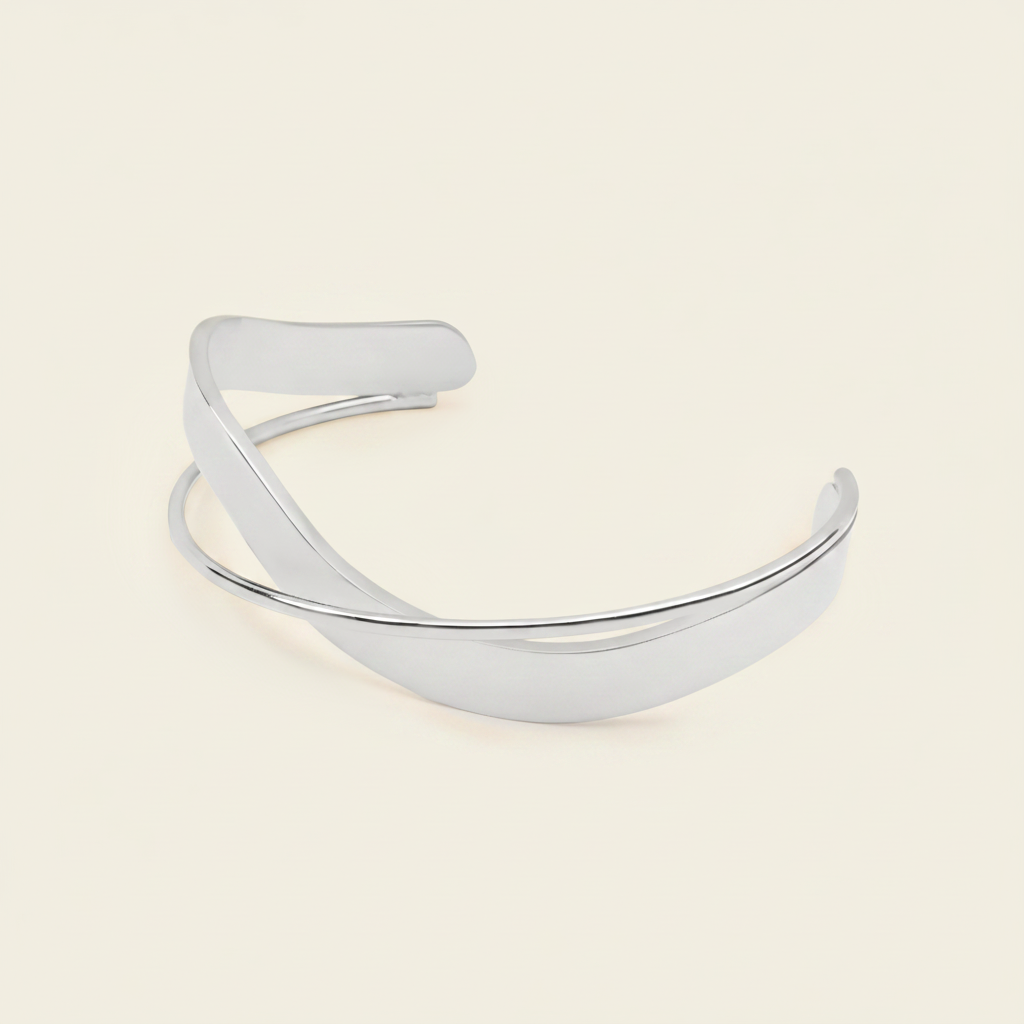 A polished silver-toned metal cuff bracelet with a smooth, curved open design, displayed on a solid light beige background.