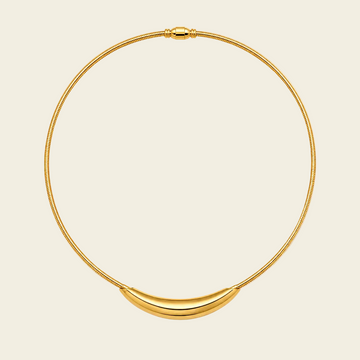 A gold snake-chain necklace with a polished crescent-shaped pendant, displayed on a light cream background.
