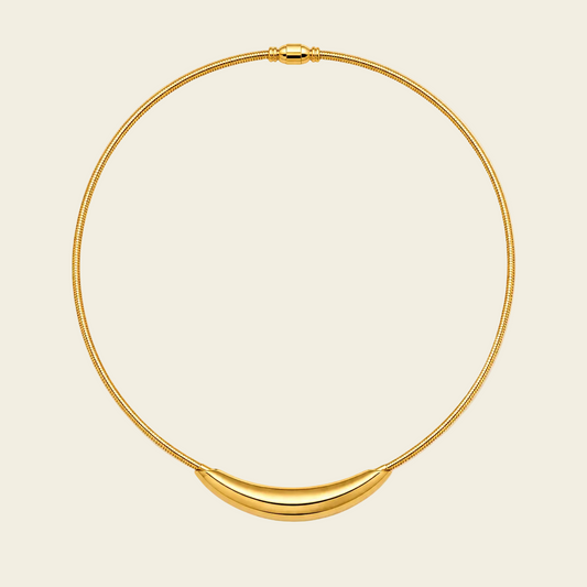 A gold snake-chain necklace with a polished crescent-shaped pendant, displayed on a light cream background.