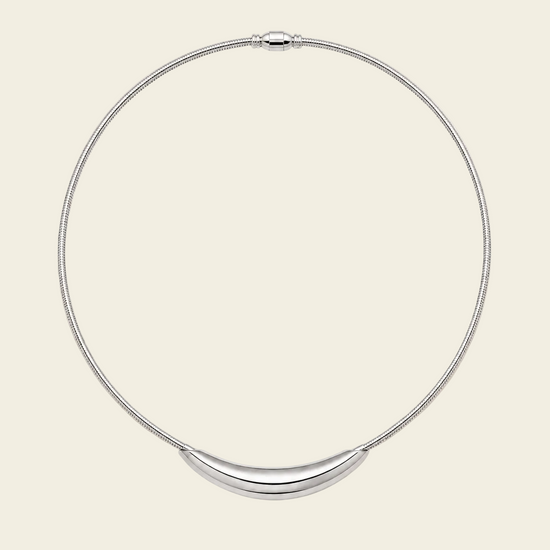 A silver snake chain necklace with a curved, polished silver bar pendant, displayed on a solid light beige background.