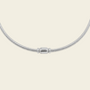 A silver snake chain necklace with a polished cylindrical clasp, displayed against a solid pale peach background.