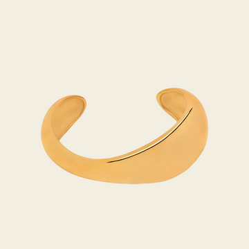 A minimalist, curved open cuff bracelet in a matte gold finish, displayed on a light cream background.