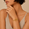 Woman wearing a gold bracelet with a knot design on a beige background