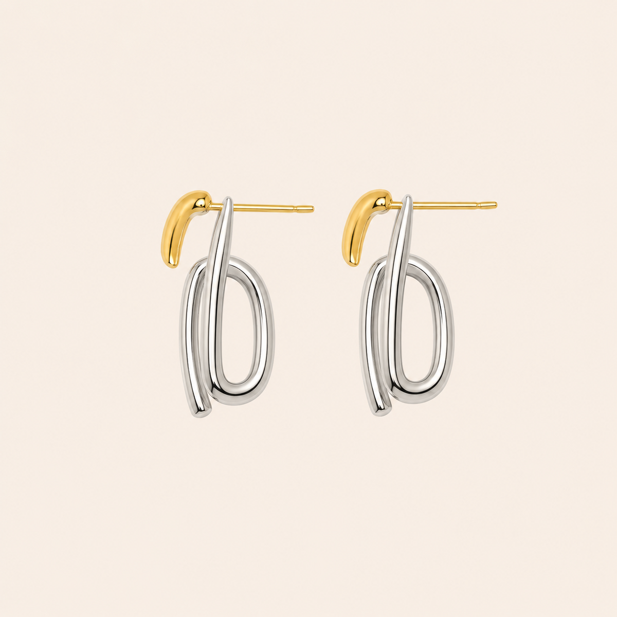 A pair of modern abstract dangle earrings featuring polished silver-toned loops and a small gold-toned post, displayed on a solid light beige background.